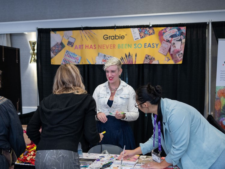 People interacting at an arts and crafts booth featuring painting supplies and colorful art materials.