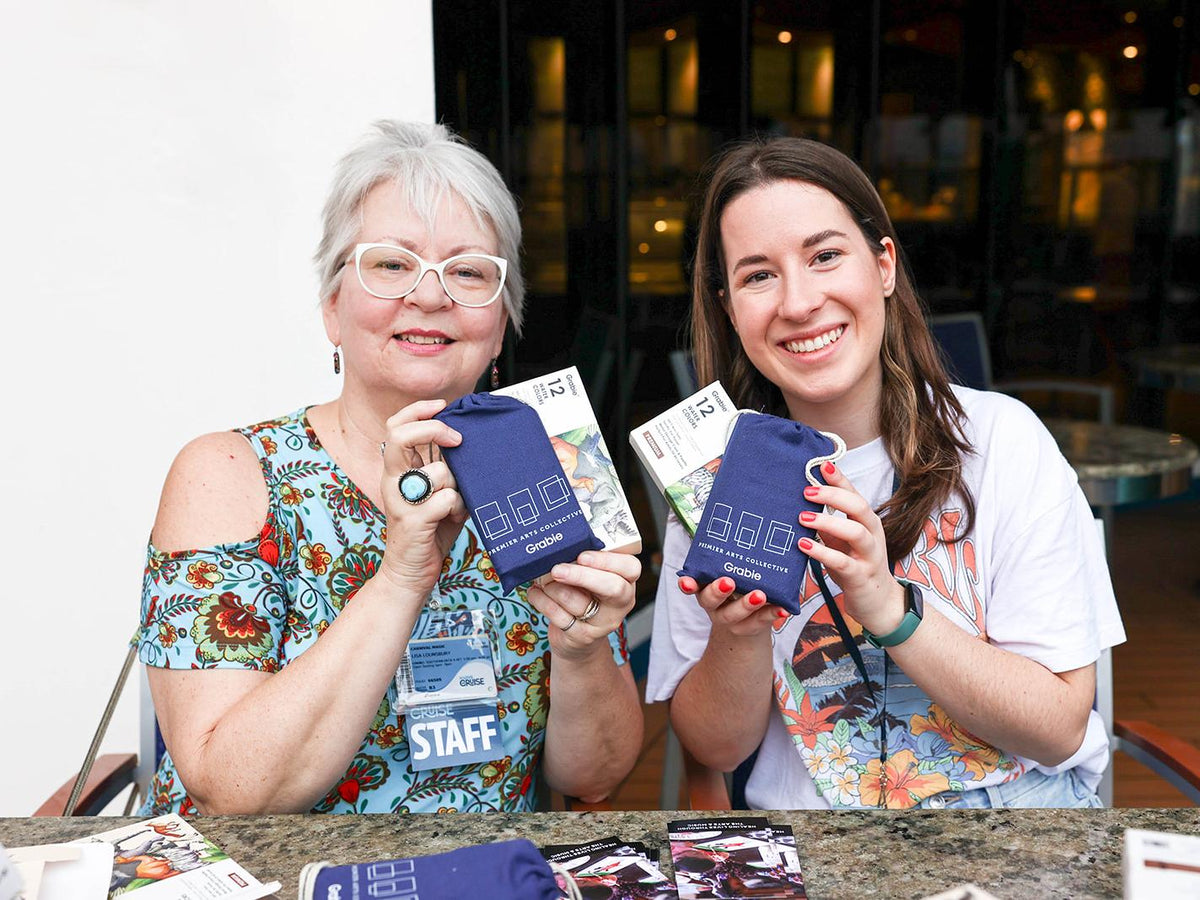 Two women holding art supply kits with colored pencils and Grabie pouches at a craft event.