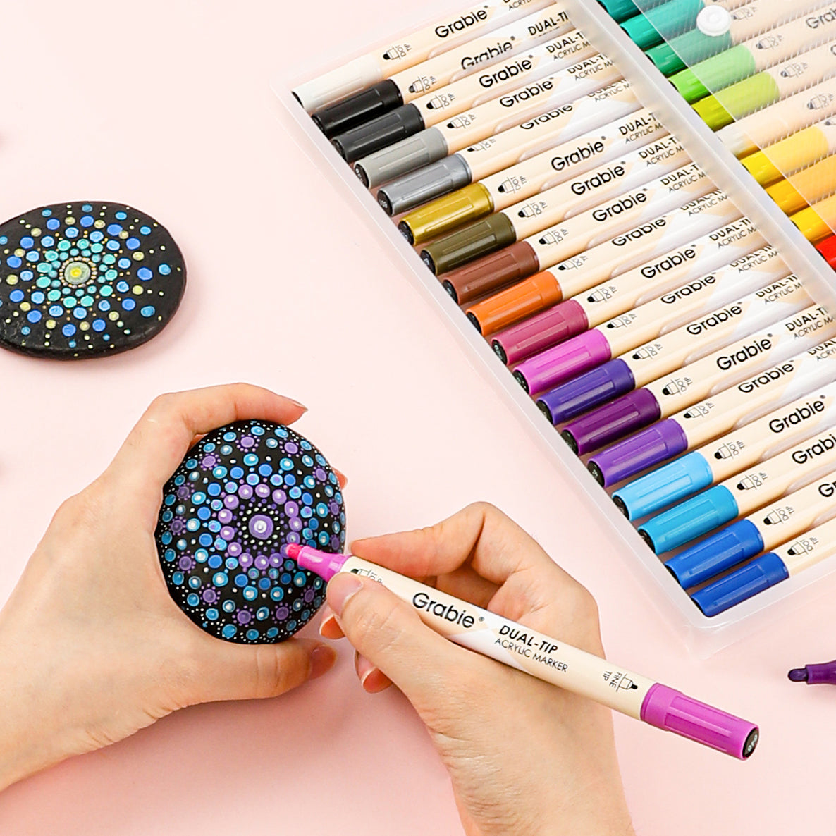 Hand drawing colorful dot mandala art on stone with acrylic paint pens and markers set.