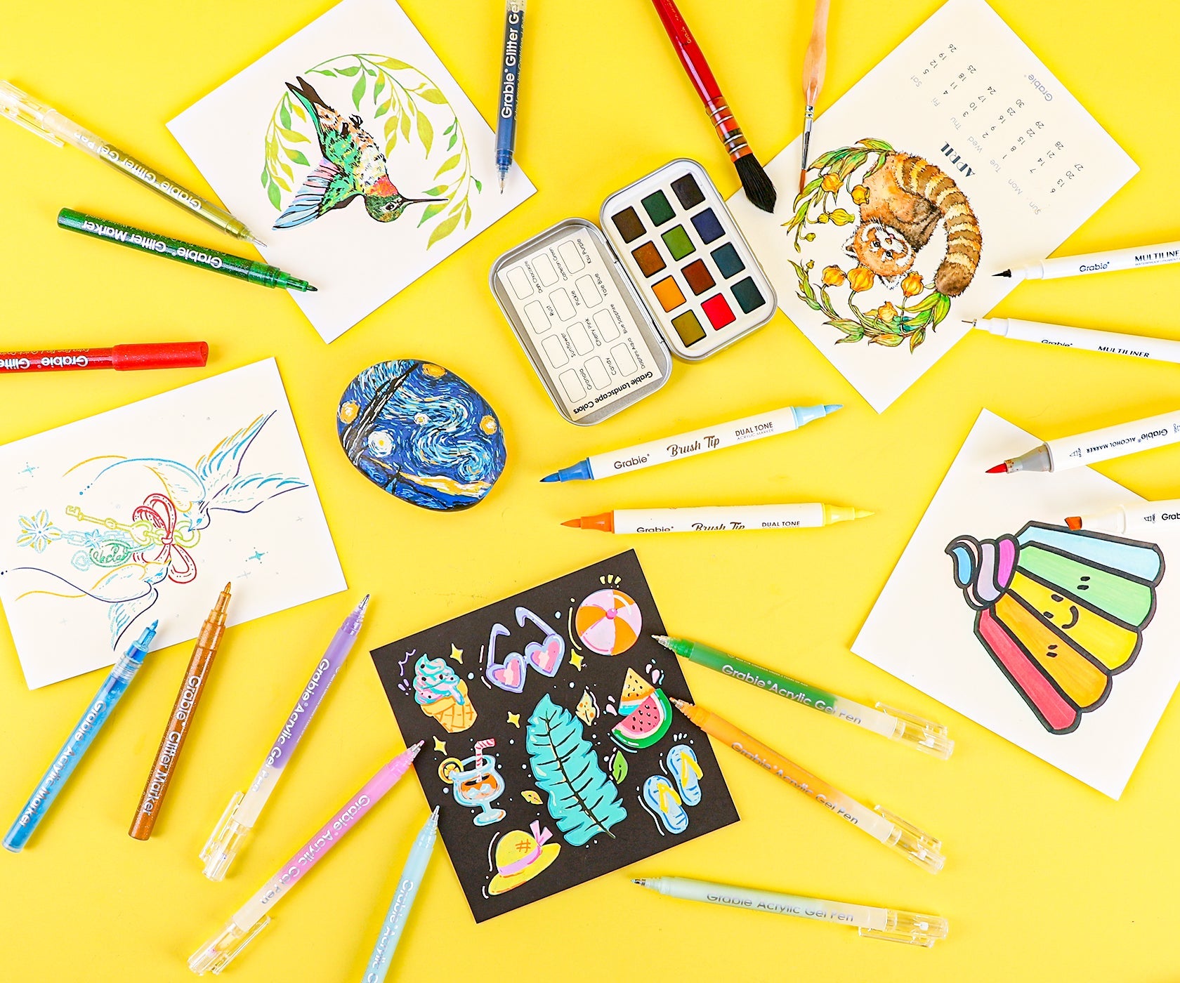 Assorted art supplies including watercolor palette, drawing pens, colored pastels, and sketchbook on a yellow background