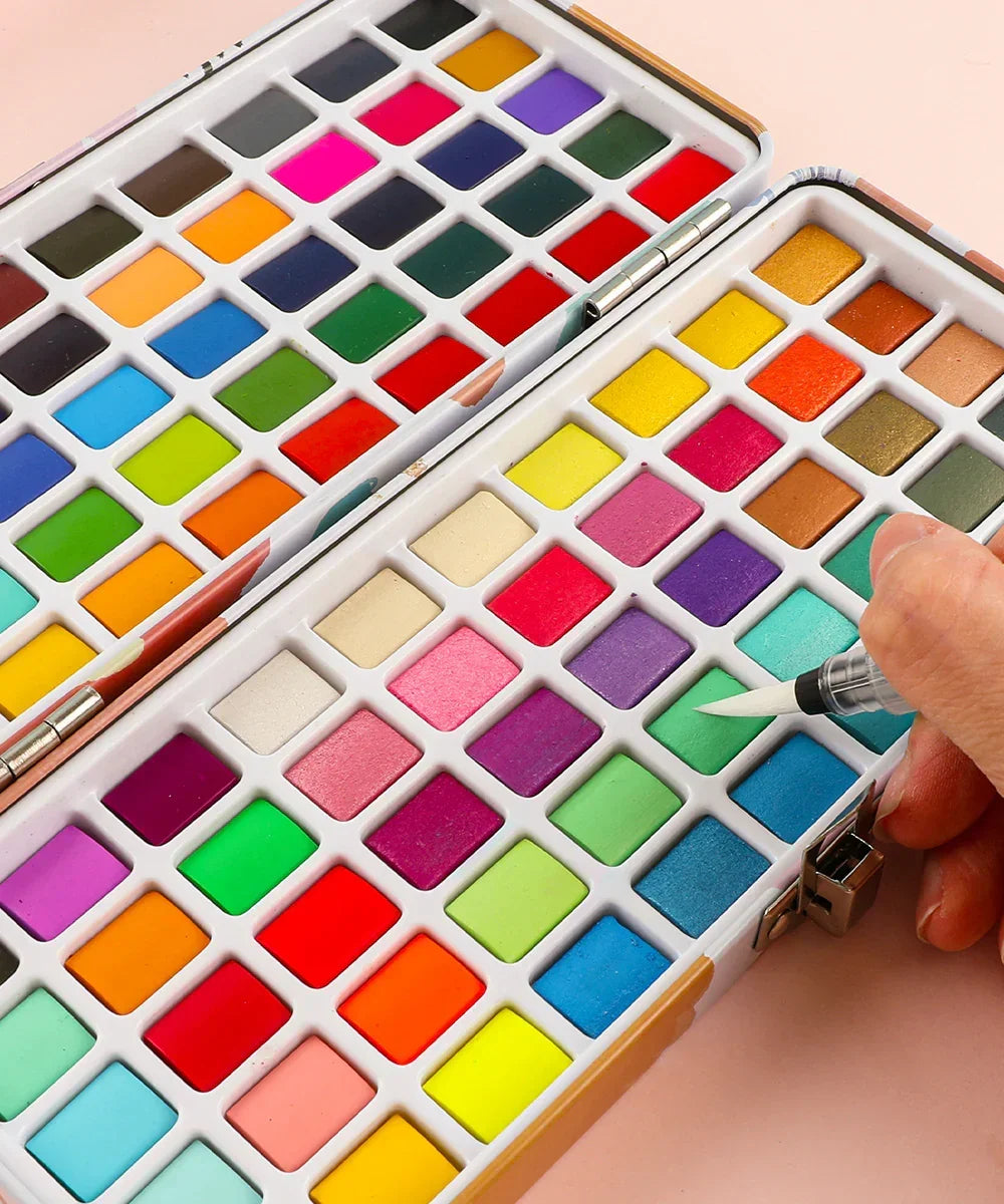 Watercolor Travel Set of 100 With Brush showing vibrant colors and a hand using a brush on a blue shade palette