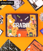 Halloween-Themed Grabie Scrapbook Club Box with spooky designs and art supplies laid out on an orange background