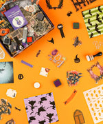 Halloween-Themed Grabie Scrapbook Club Box with stamps, ink pads, themed stickers, and decorative paper for crafting and scrapbooking.