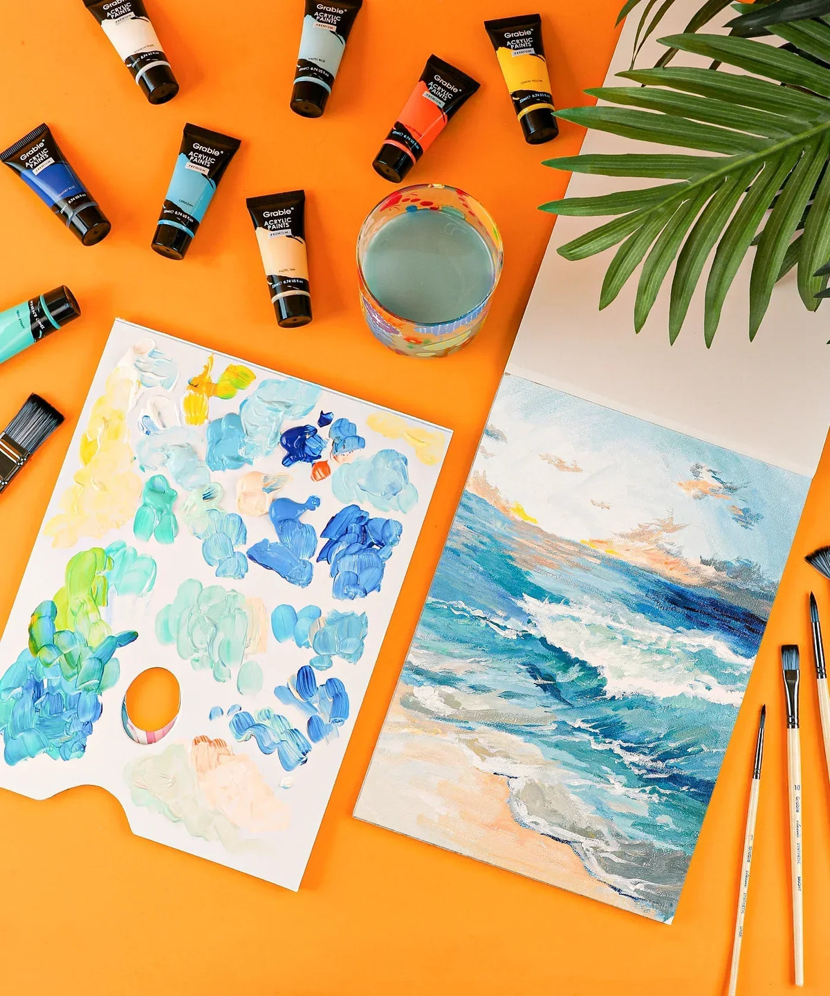 Premium Acrylic Paint Set - 22ml Tubes with a palette, paintbrushes, glass of water, and ocean-themed artwork on orange background