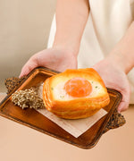 Hands holding a tray with a realistic Feel-Good Stress Relief Foam Squishy - Fried Egg Bun toy and decorative dried flowers