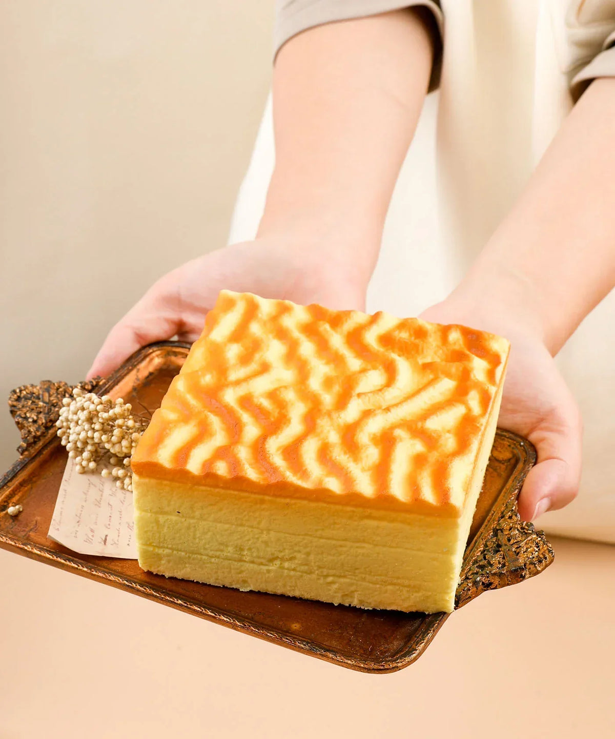 Hands holding a tray with a yellow squishy foam dessert featuring a tiger skin pattern, Feel-Good Stress Relief Foam Squishy - Tiger Skin Cake