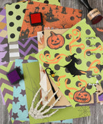 16 Sheets Grabie Exclusive Halloween Party Paper Set with spooky designs, skeleton hand, ink pads, and decorative clips on wood surface