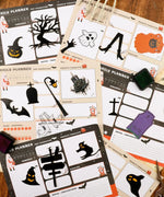 30 sheets Halloween Exclusive Daily Planner with spooky icons and decorative stamps laid out on a wooden surface