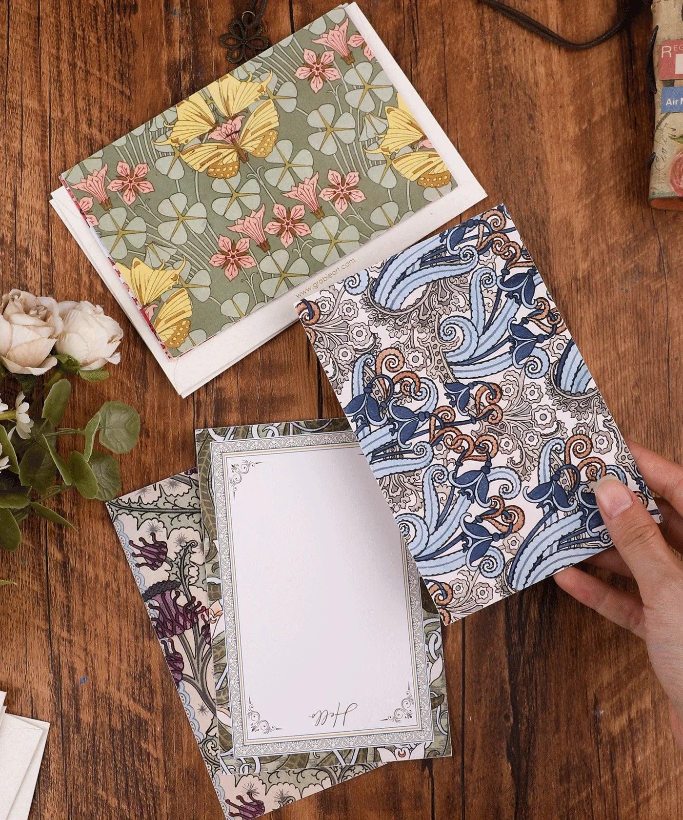 6 Pack Postcards With 6 Matching Envelopes featuring floral and abstract designs on a wooden table with flowers nearby
