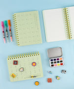 2-IN-1 POPIN Notebook with art supplies including markers, watercolor set, and decorative pins on a blue surface