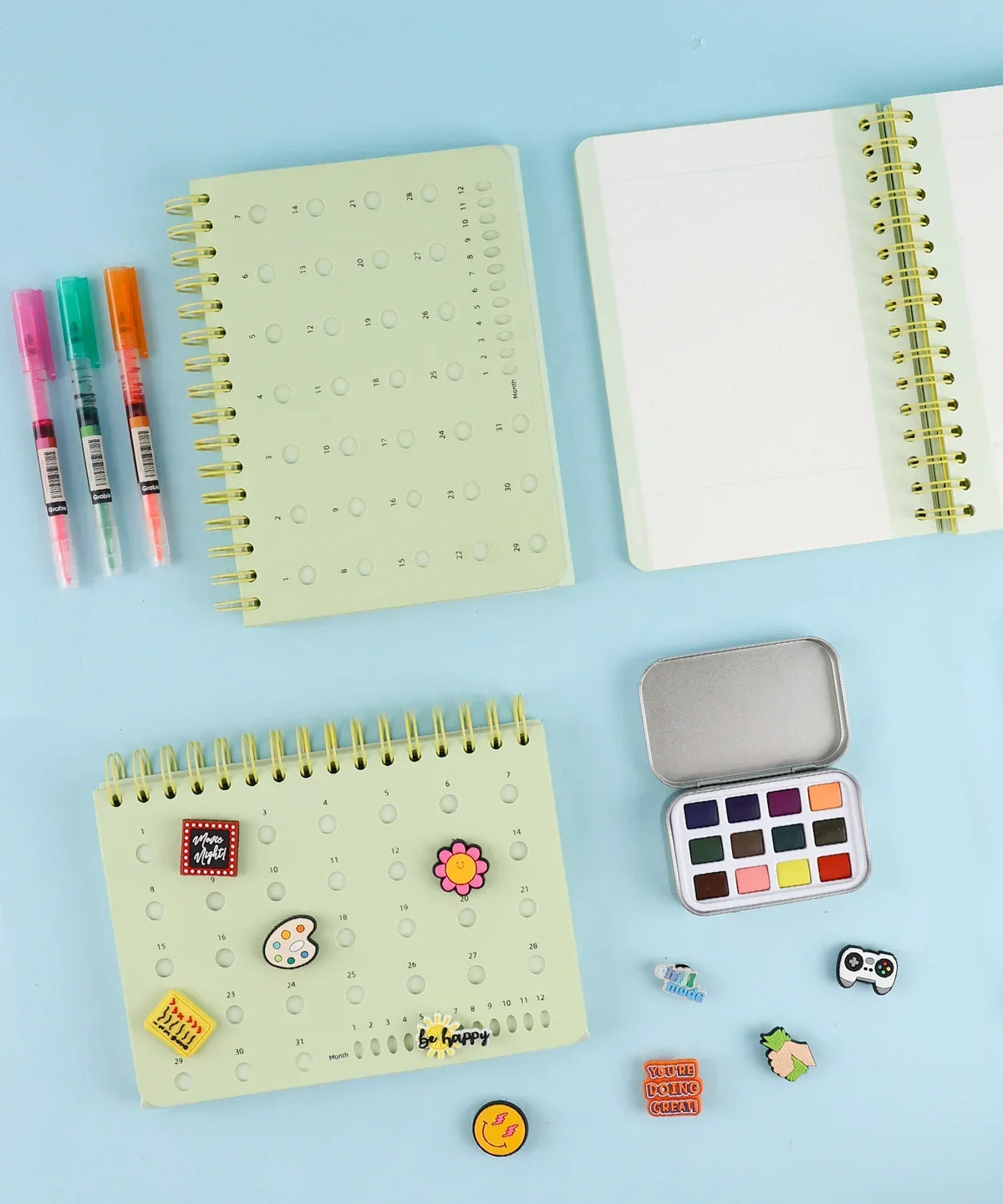 2-IN-1 POPIN Notebook with art supplies including markers, watercolor set, and decorative pins on a blue surface