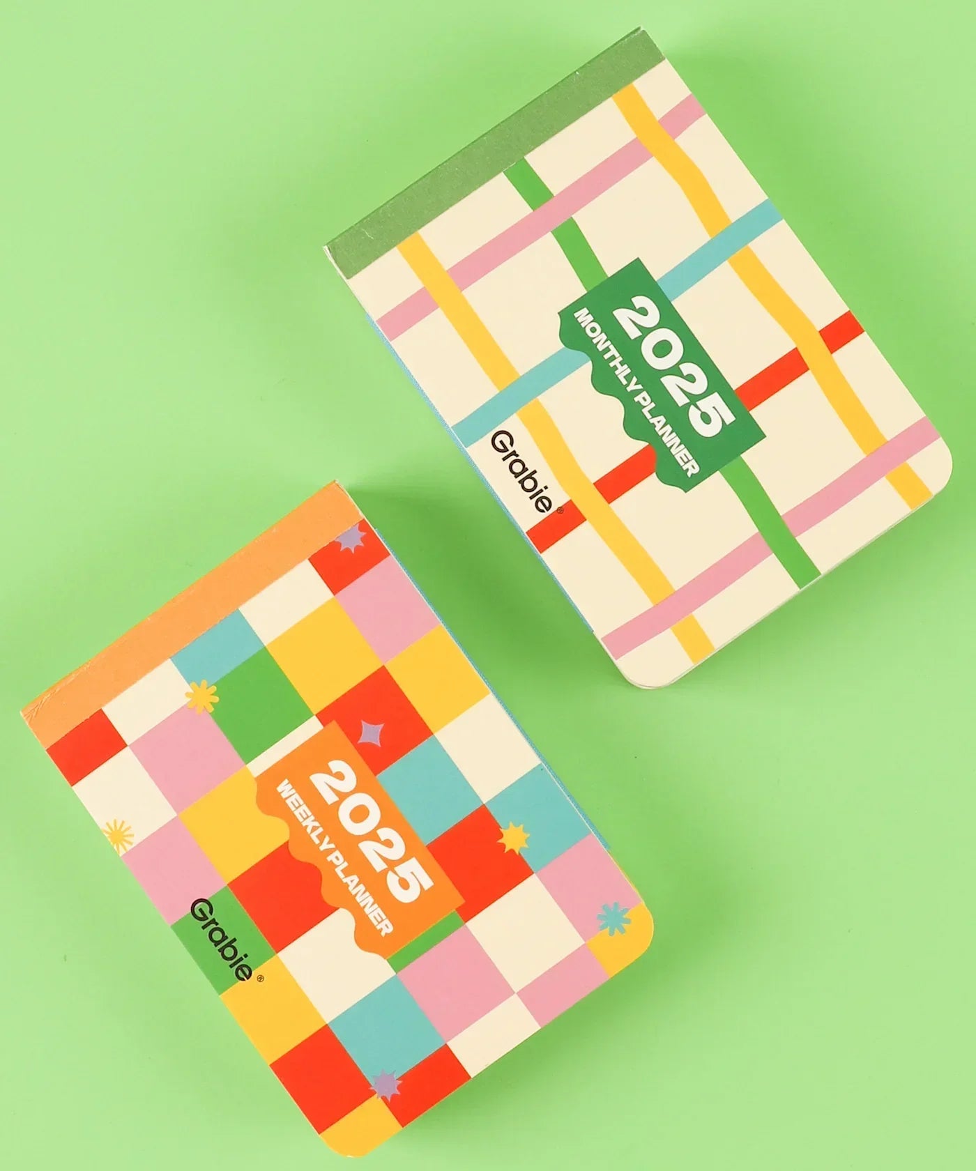 Two colorful planners with patterned covers labeled 2-IN-1 2025 Monthly & Weekly Planner on a green background