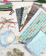 Cozy Pop Stores-Themed Grabie Scrapbook Club Box with patterned papers, decorative cutouts, and crafting supplies for scrapbooking.