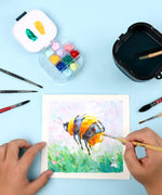 3-in-1 Paint Brush Cleaner Bucket with brushes beside watercolor painting of a bee and palette on blue surface