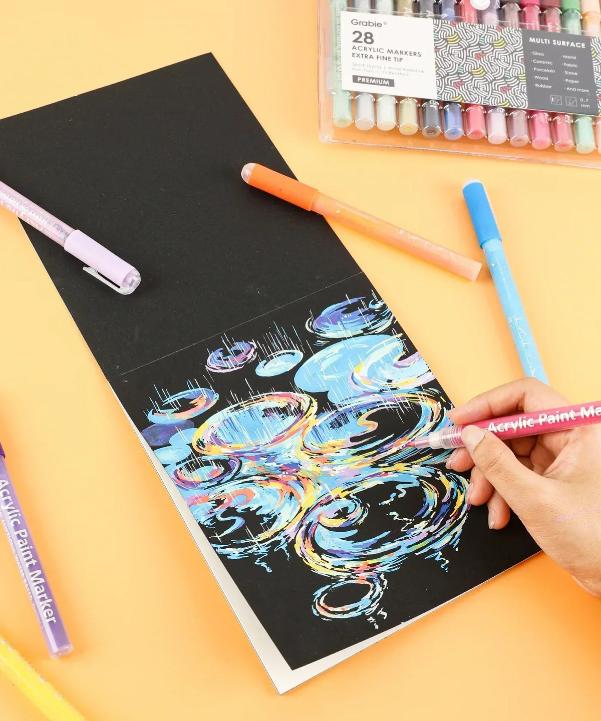 Extra Fine Tip Acrylic Paint Marker Set of 28 used to create vibrant art on black paper with detailed colorful swirls.