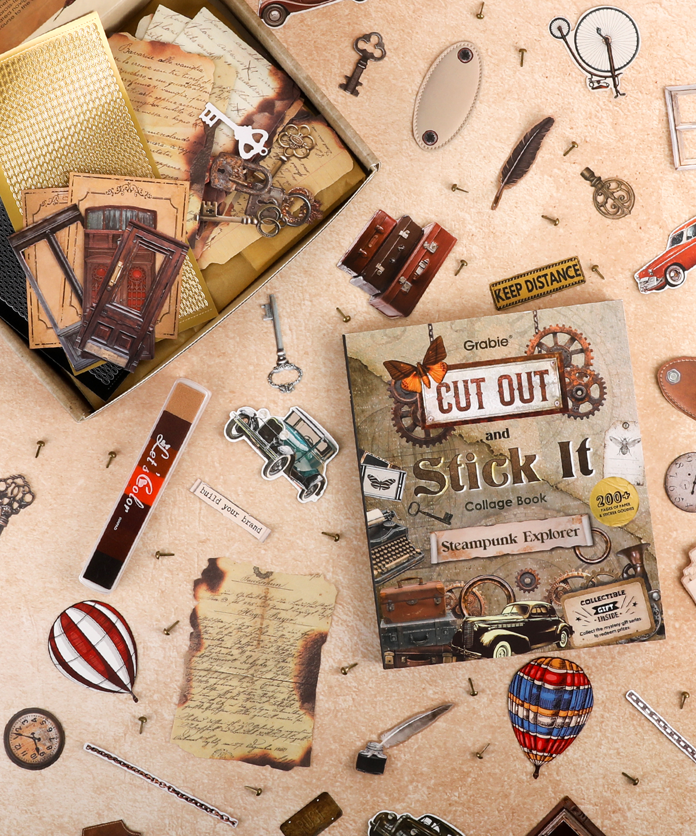 Steampunk Explorer-Themed Grabie Scrapbook Club Box with vintage keys, hot air balloons, and collage art supplies scattered on table