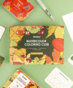 Autumn-Themed Watercolor Coloring Club Box with vibrant fall leaves, berries, and art supplies on green background