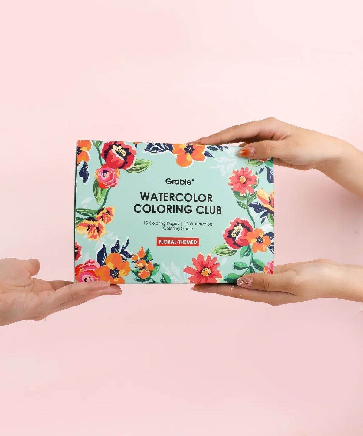 Hands exchanging the Floral-Themed Watercolor Coloring Club Box with bright floral artwork on a pastel background