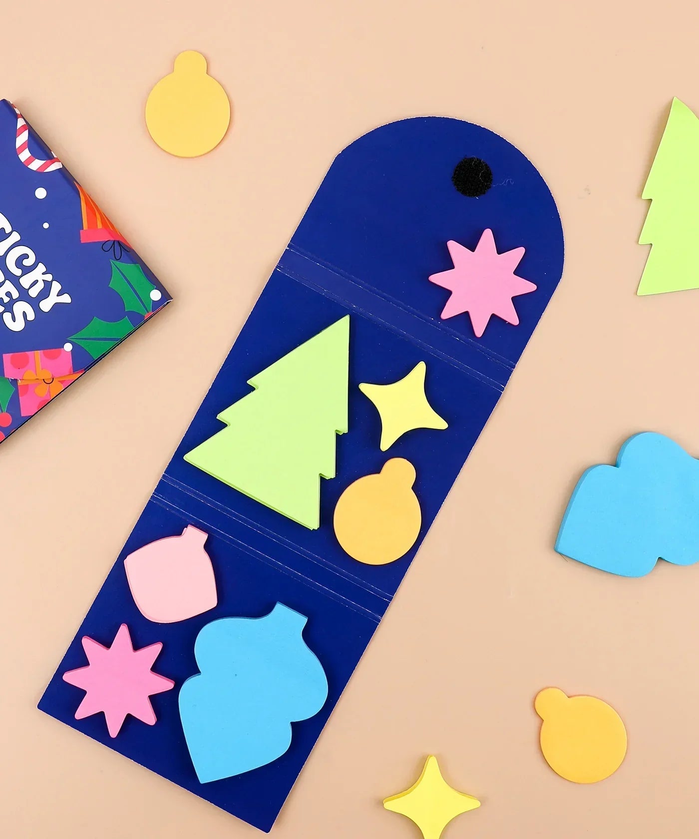 Colorful holiday-shaped sticky notes arranged inside a blue holder for A Pocket Full Of Happiness Sticky Notes