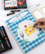 Person coloring a cake illustration with oil pastels in the Let Your Feelings Flow 30-Day Workbook