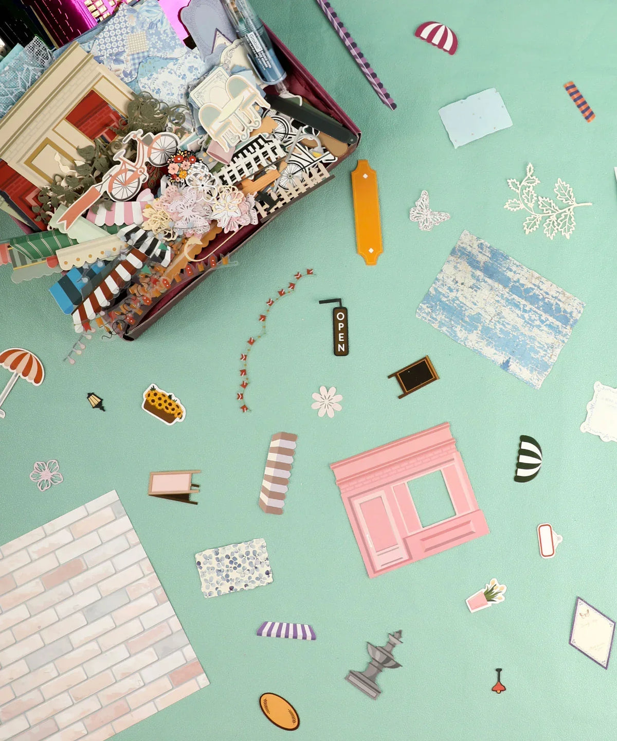 Cozy Pop Stores-Themed Grabie Scrapbook Club Box with decorative scrapbook stickers and art supplies scattered on turquoise background