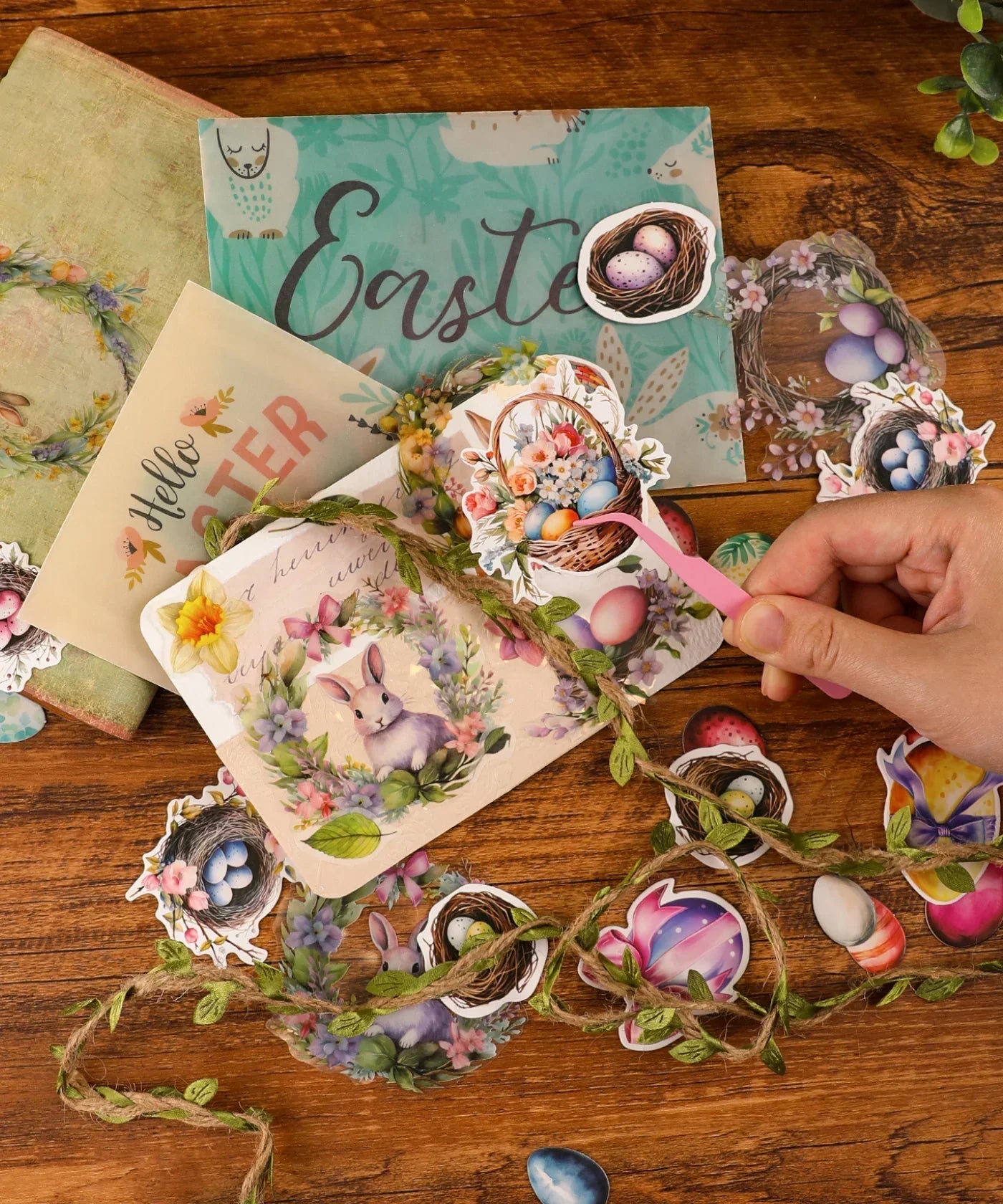 Hand arranging colorful Easter-themed scrapbook cutouts and wreath with twine in Easter-Themed Grabie Scrapbook Club Box