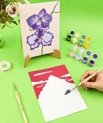 Paint-by-Number Nature Series Kit - 2 Designs showing floral and mountain paintings with brushes and paint pots on green background