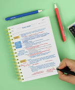 Person writing colorful notes on paper with Medium Point Erasable Gel Pen Set including blue and red pens on green surface