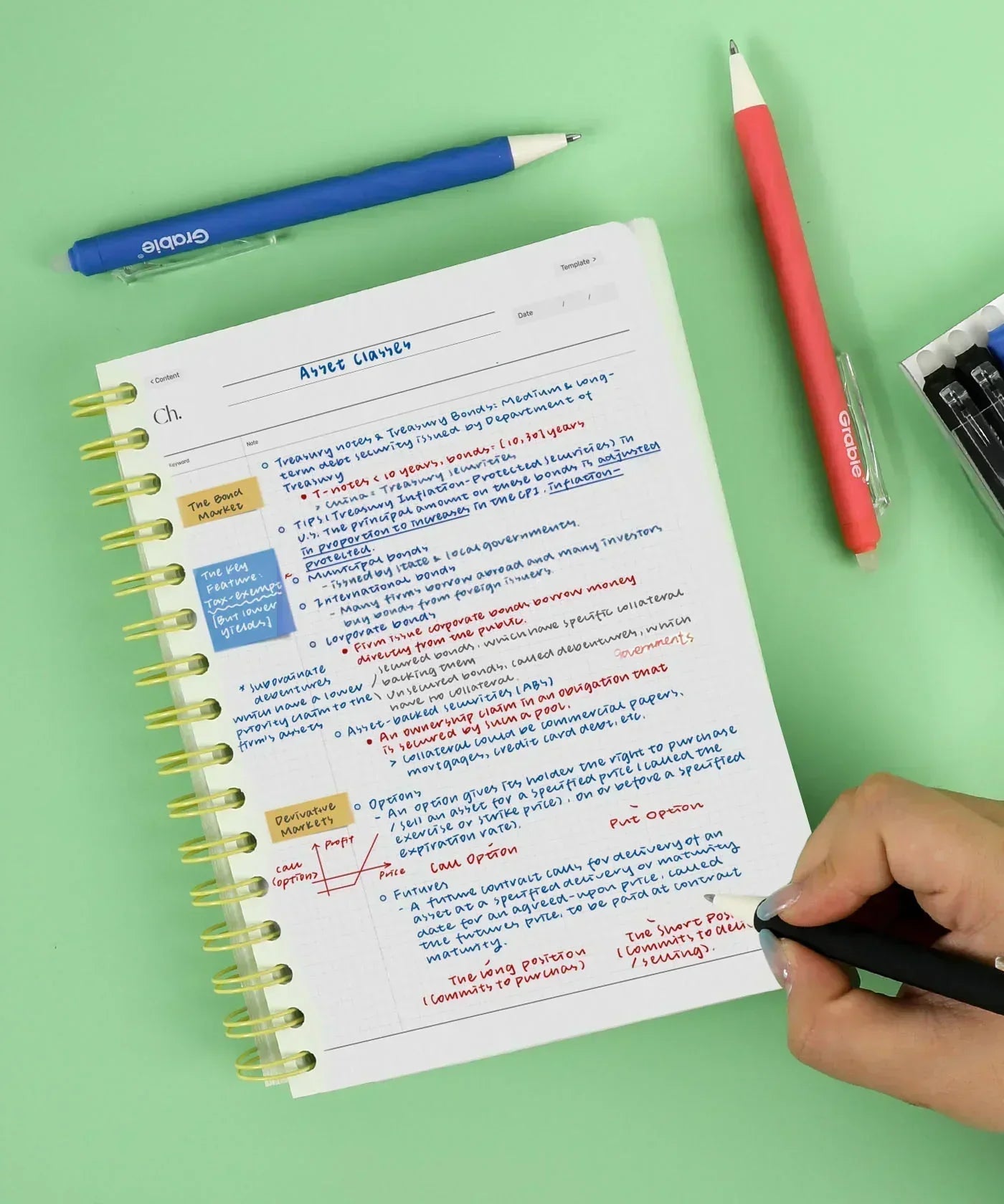 Person writing colorful notes on paper with Medium Point Erasable Gel Pen Set including blue and red pens on green surface