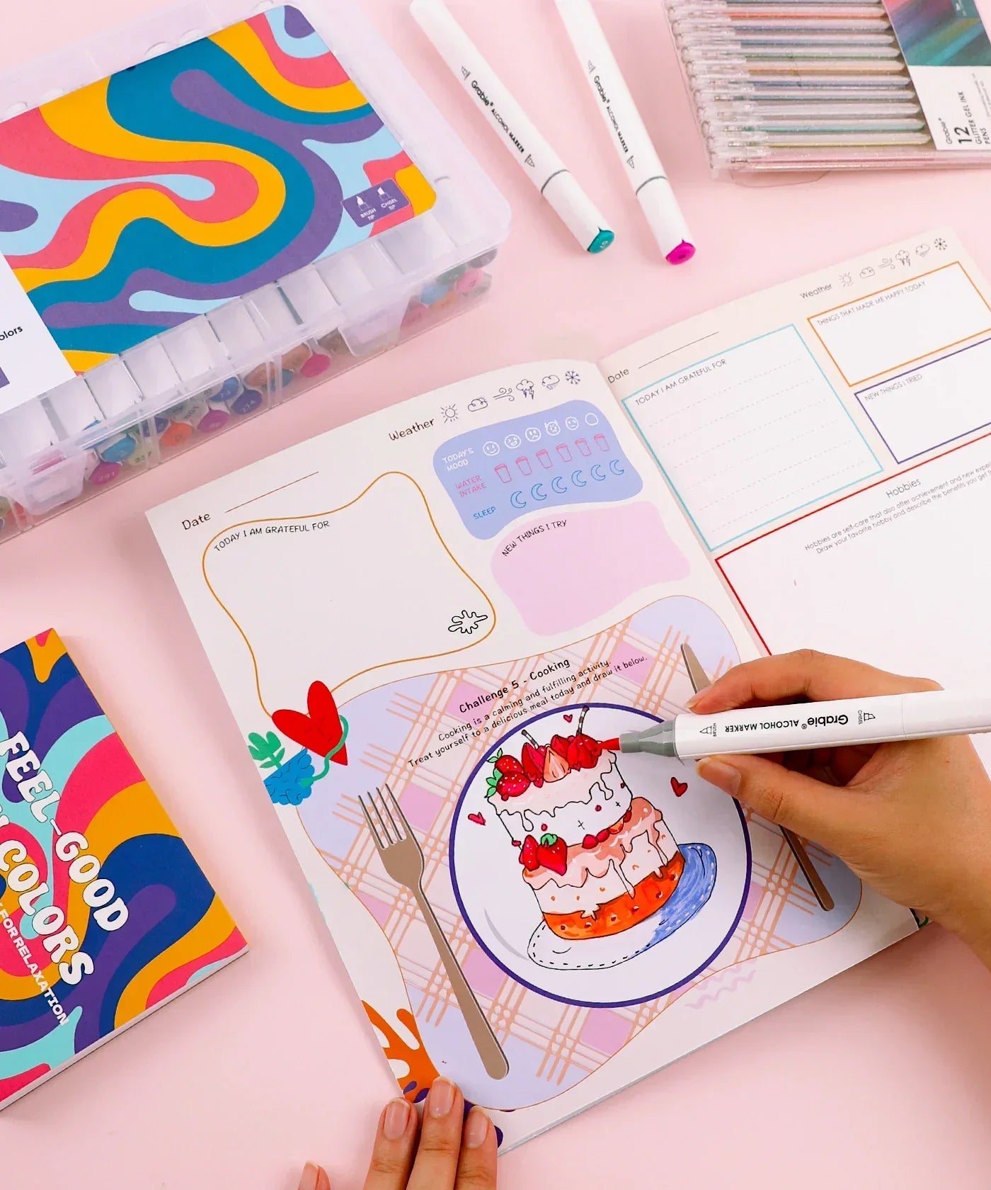 Person coloring a strawberry cake illustration in the Be You And Love You 28-day Workbook with markers and pens nearby