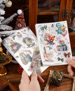 Hands holding 8 Sheets Grabie Exclusive New Year Sticker Set with festive gift and holiday designs on wooden table.