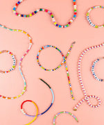 Colorful handmade beaded jewelry including bracelets and necklaces with letters on a pink background featuring Grabie Bead Box