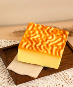 Feel-Good Stress Relief Foam Squishy - Tiger Skin Cake with textured golden top on wooden tray and cloth background
