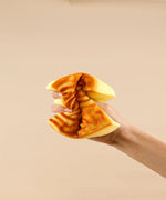 Hand squeezing a soft foam toy shaped like a tiger-striped cake labeled Feel-Good Stress Relief Foam Squishy - Tiger Skin Cake