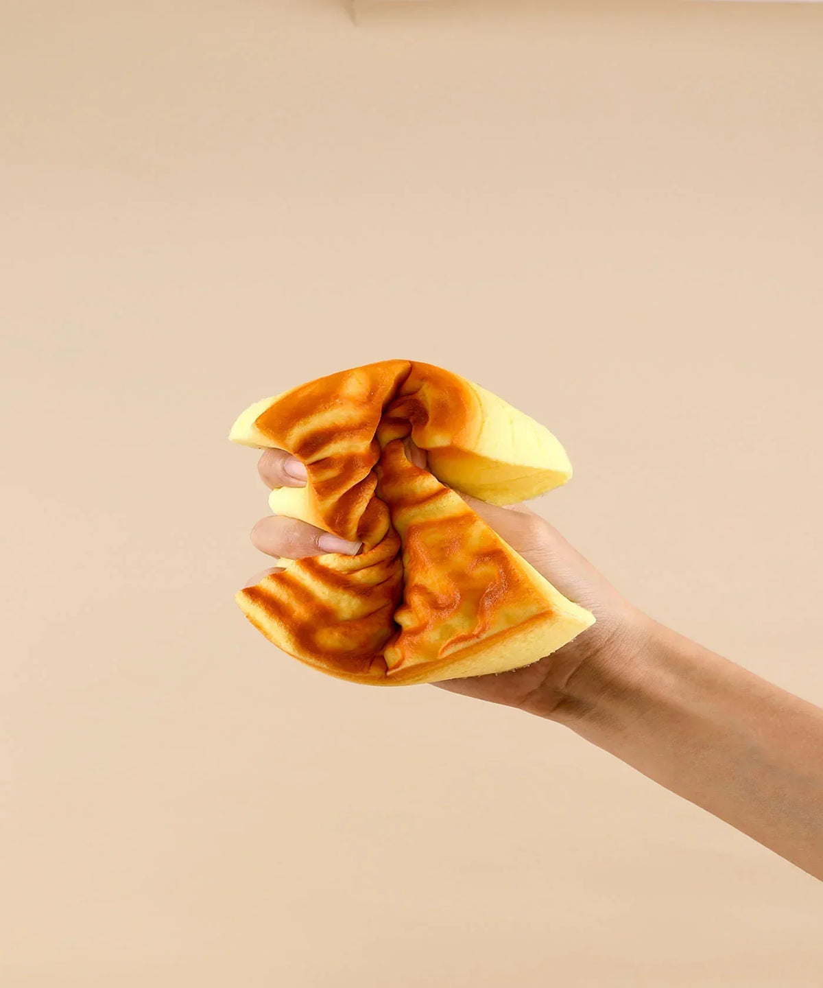 Hand squeezing a soft foam toy shaped like a tiger-striped cake labeled Feel-Good Stress Relief Foam Squishy - Tiger Skin Cake
