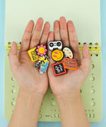 Hands holding colorful decorative pins with positive messages and icons on a 2-IN-1 POPIN Notebook background