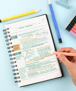 Hand holding a pen writing colorful notes in a spiral notebook alongside the Medium Point Erasable Gel Pen Set and pencils.