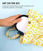 Hand placing 3-in-1 Paint Brush Cleaner Bucket into a yellow patterned portable bag for art on the go