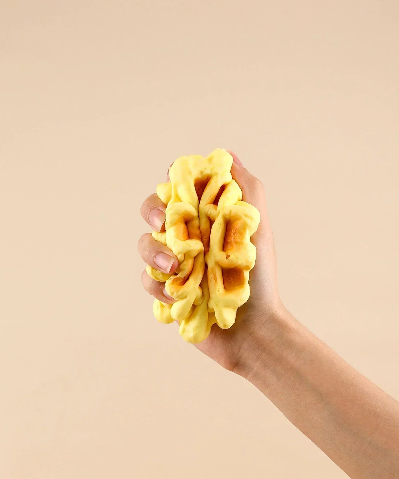 Hand squeezing a soft yellow foam waffle toy designed as Feel-Good Stress Relief Foam Squishy - Waffle Sandwich