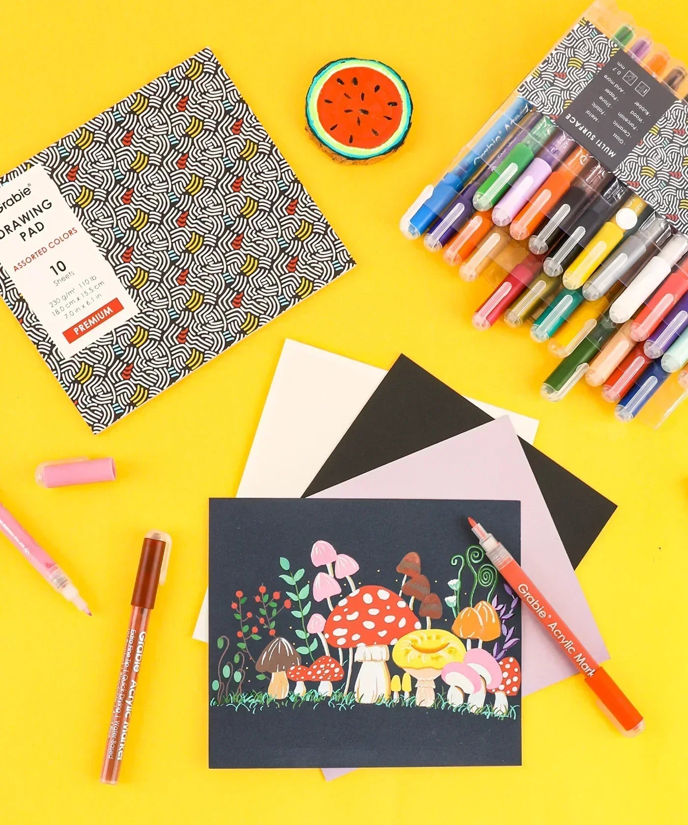 Extra Fine Tip Acrylic Paint Marker Set of 28 displayed with illustrated mushroom artwork, pens, and drawing pad on yellow background