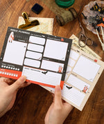 Hands holding 30 sheets Halloween Exclusive Daily Planner with Halloween-themed design on wooden desk background