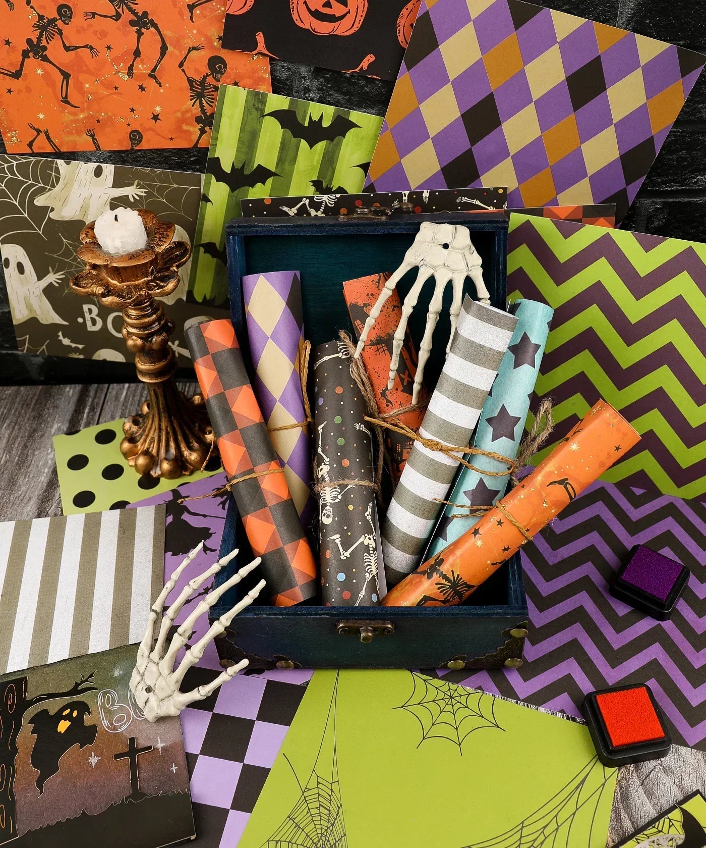 Colorful Halloween-themed papers with skeleton hands and ink pads in a dark setting featuring 16 Sheets Grabie Exclusive Halloween Party Paper Set