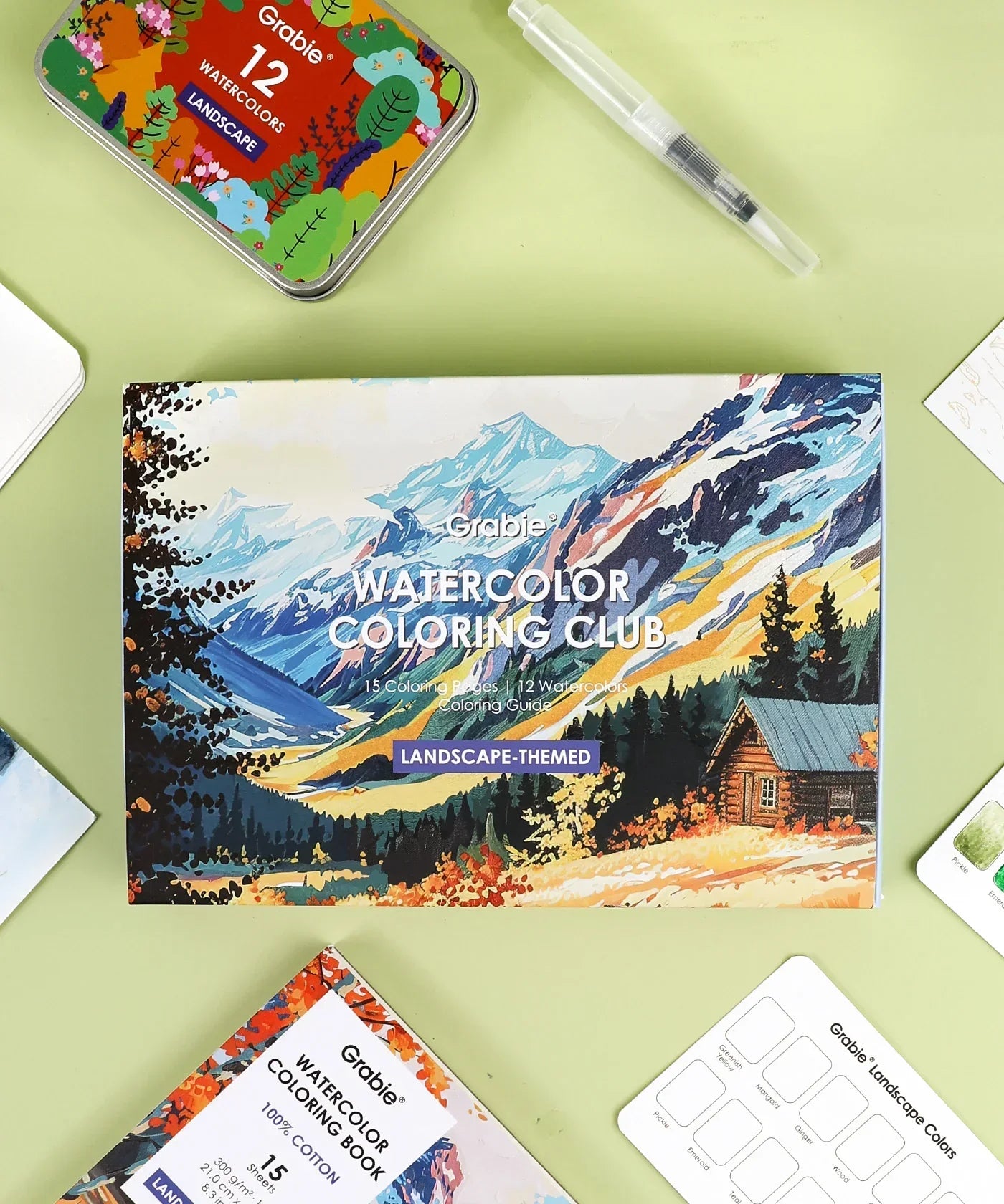 Landscape-Themed Watercolor Coloring Club Box with art supplies including watercolors and brush on green background