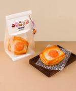 Feel-Good Stress Relief Foam Squishy - Fried Egg Bun displayed on wooden tray with cute bakery packaging nearby.