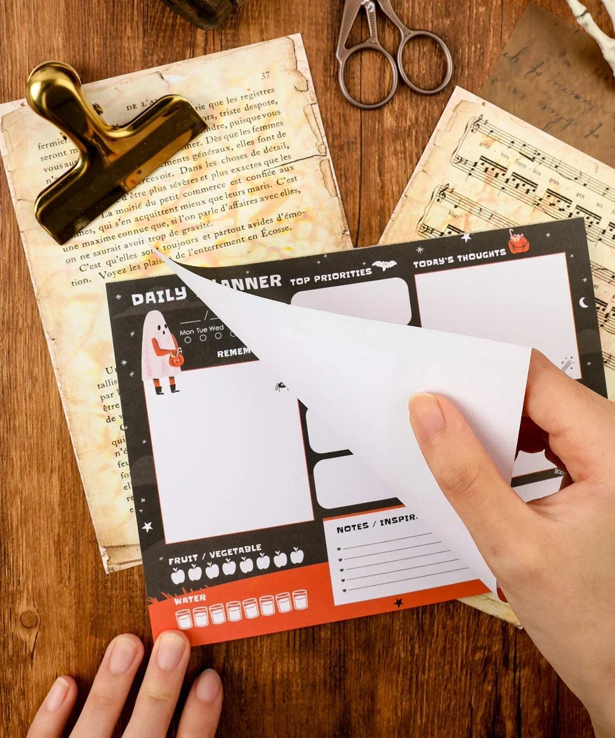Person flipping a page of the 30 sheets Halloween Exclusive Daily Planner with Halloween-themed sections and icons.