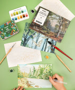 Forest-Themed Watercolor Coloring Club Box with paints, brushes, and watercolor art of forest landscapes in progress