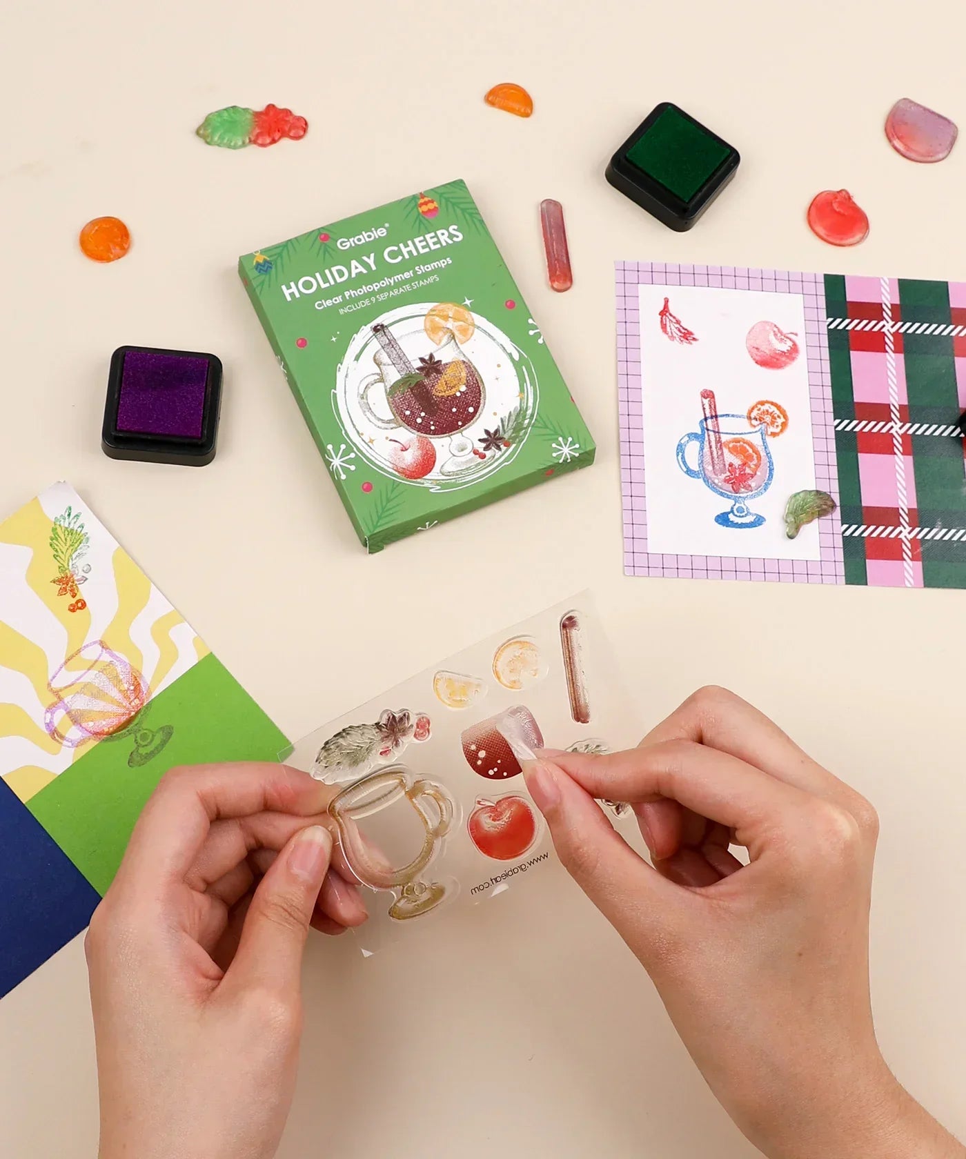 Hands using Holiday Cheers Clear Photopolymer Stamps with ink pads and colorful stamped holiday-themed designs on paper