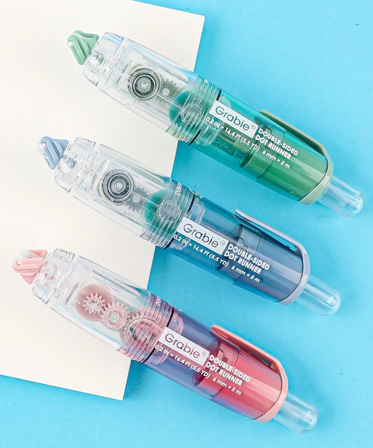 Three colorful Double-Sided Adhesive Dot Runners for scrapbooking and art supplies on a blue background