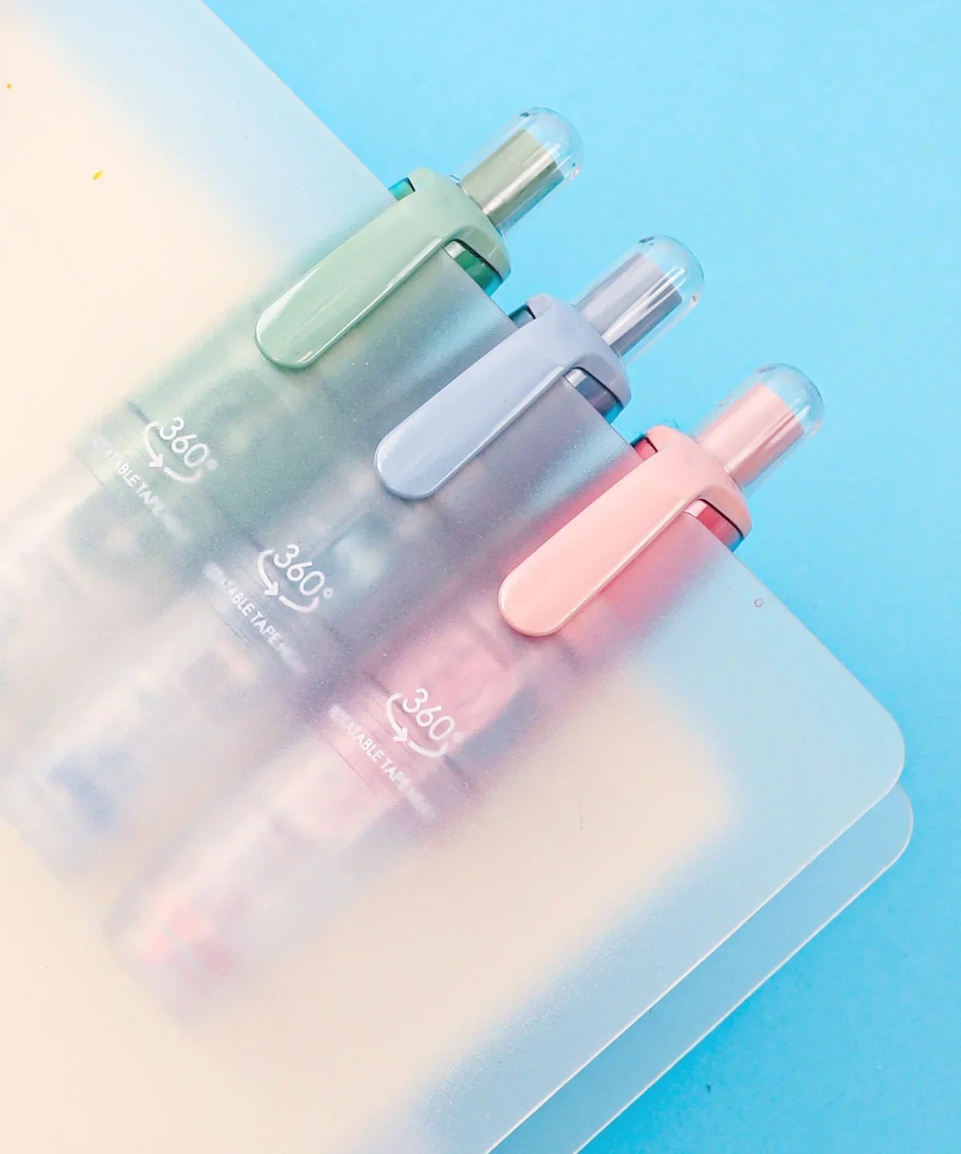 Three pastel-colored Double-Sided Adhesive Dot Runner tools clipped to translucent folders on a blue background