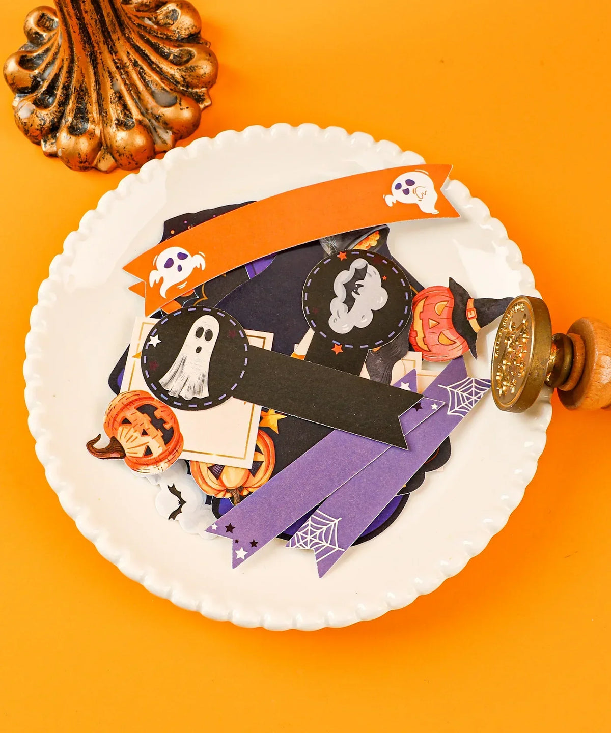 Halloween-Themed Grabie Scrapbook Club Box with ghost, pumpkin, and spider web paper embellishments on a white plate